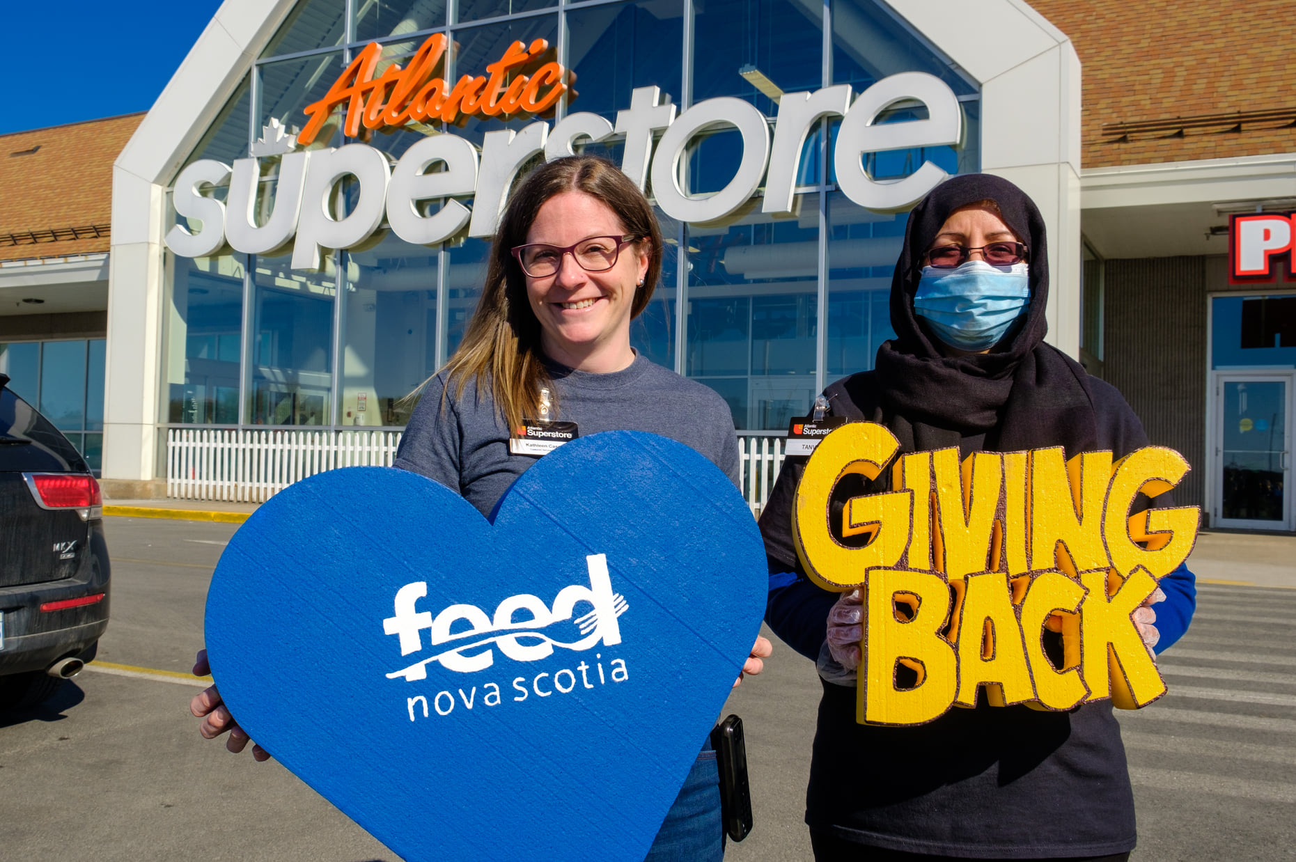 Two women stand in front of a Loblaws store with a Feed Nova Scotia sign